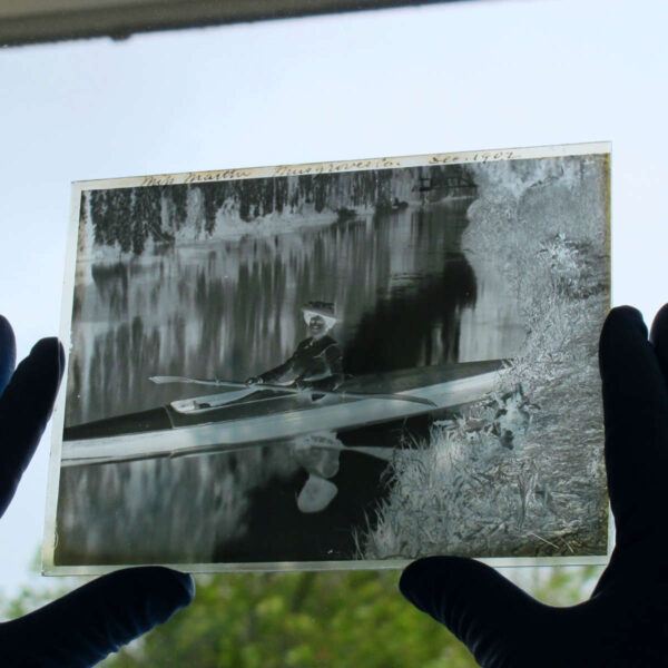 Glass plate negative held up to light showing a negative photograph of a Victorian woman by a river bank